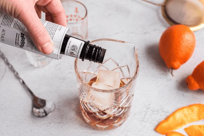 Bartender khuấy Manhattan cocktail trong mixing glass với vermouth và Angostura bitters