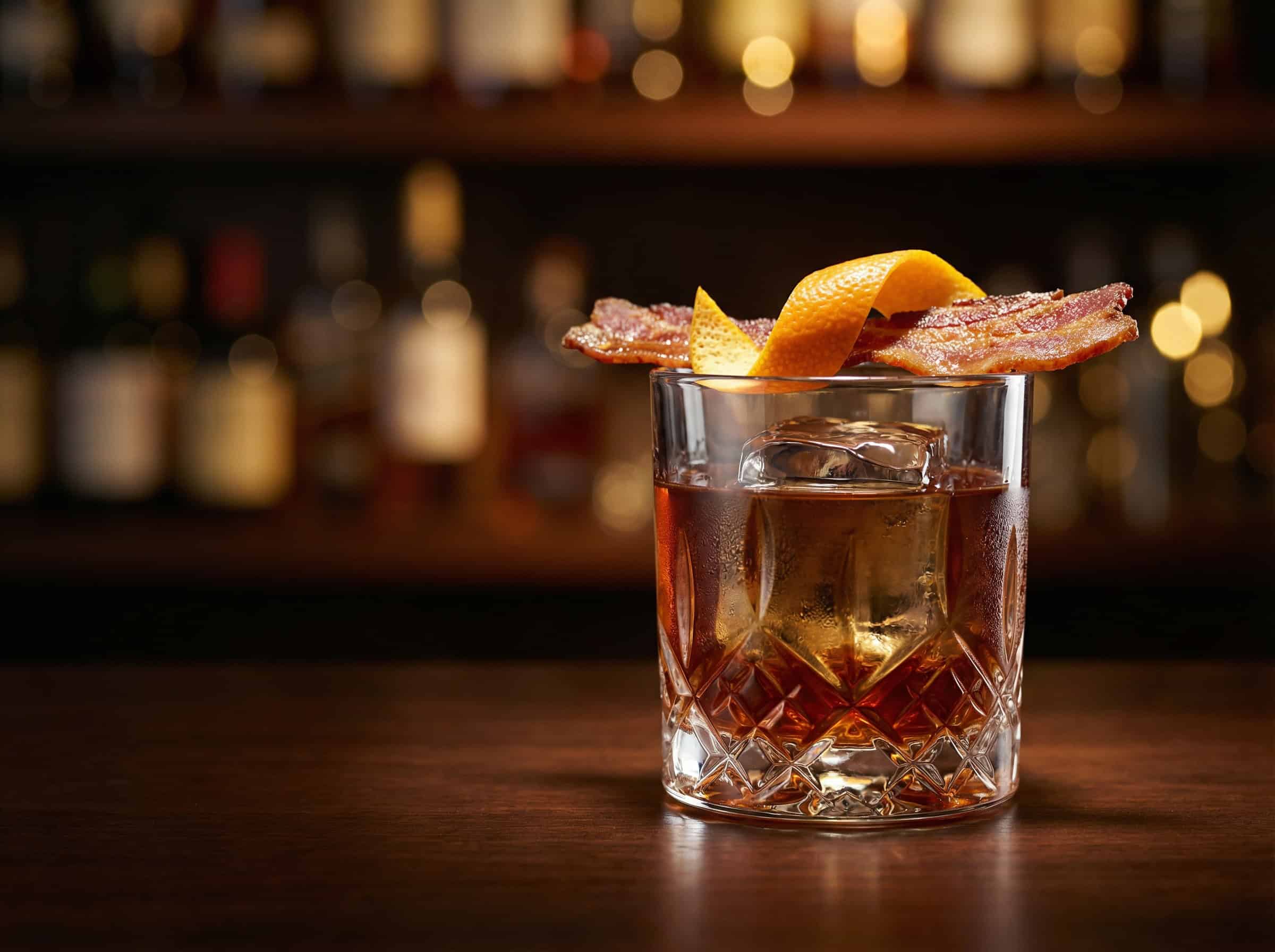 Bacon Old Fashioned cocktail trong ly rocks với thanh bourbon đóng băng và thịt xông khói — công thức pha chế chuẩn bar