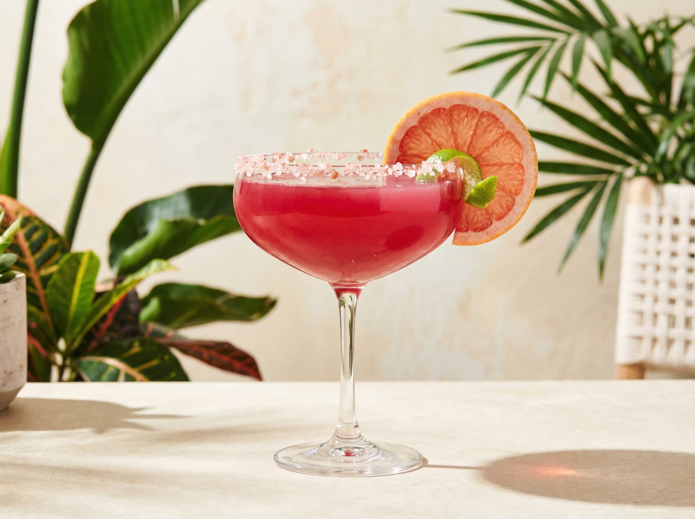 Grapefruit Skinny Margarita màu hồng-ruby đậm trong coupe glass với muối Himalaya và lát bưởi hồng