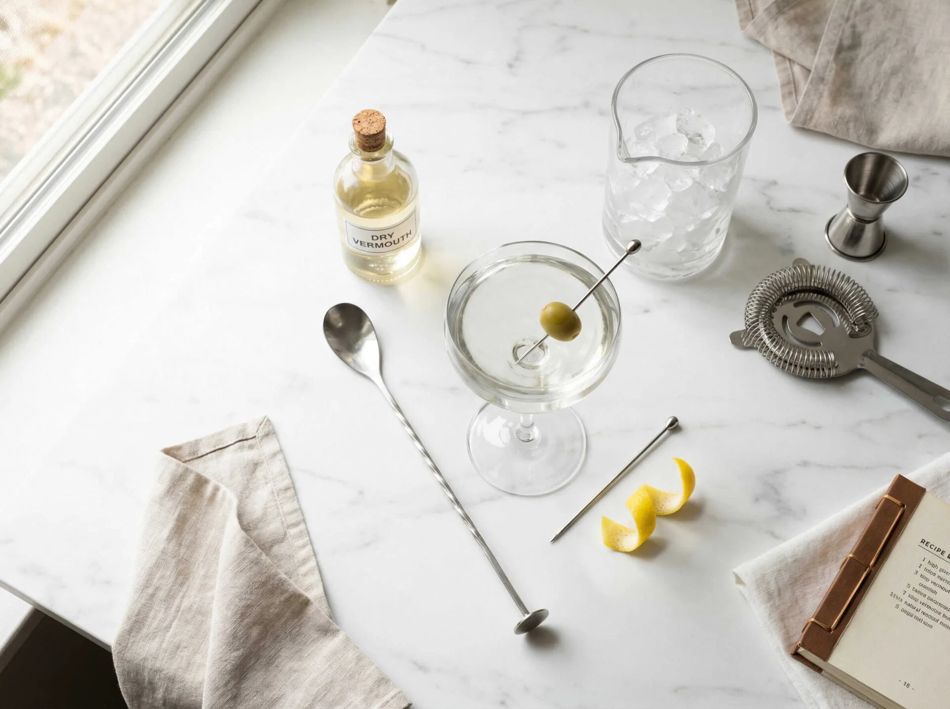 Dụng cụ pha Martini từ trên xuống: mixing glass, bar spoon, ly Martini, chai vermouth, olive và vỏ chanh